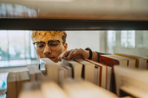 Junger Mann mit Brille sucht ein Buch in der Bibliothek einer Universität - MASF29219