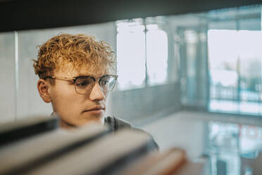 Junger Mann mit Brille in der Bibliothek einer Universität - MASF29230