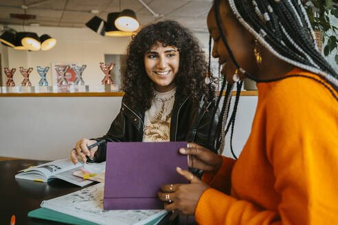 Lächelnde junge Frau, die ihren Freund beim gemeinsamen Lernen in der Universitätscafeteria anschaut - MASF29243