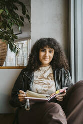 Porträt einer jungen Frau, die mit einem Buch an der Universität sitzt - MASF29253