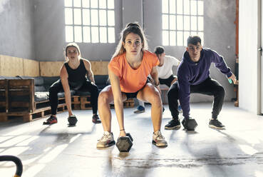 Junge Frau und Männer trainieren mit Hanteln im Fitnessstudio - JSRF01928