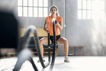 Junge Frau beim Training mit Kampfseilen im Fitnessstudio - JSRF01935