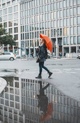 Young woman walking with orange umbrella walking on street - BFRF02406