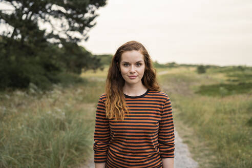 Beautiful young redhead woman standing in meadow - AKLF00527