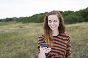 Lächelnde rothaarige Frau mit Smartphone auf einer Wiese - AKLF00532