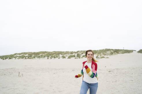 Happy young woman running on sand - AKLF00546