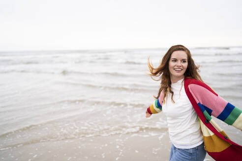 Happy young woman with arms stretched enjoying at beach - AKLF00554