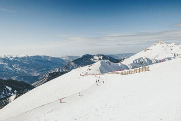 Menschen auf einem verschneiten Berg beim Skifahren im Skigebiet an einem sonnigen Tag - OMIF00732