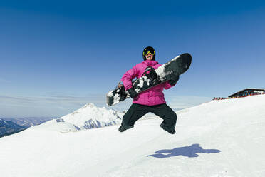 Happy man with snowboard jumping on snow in winter - OMIF00733