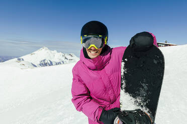 Glücklicher Mann mit Snowboard an einem sonnigen Tag - OMIF00734