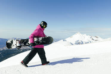 Man with snowboard walking on snowy mountain - OMIF00737