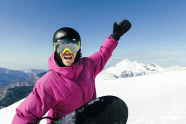 Cheerful man with hand raised enjoying at ski resort - OMIF00740