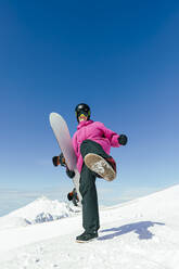 Man with snowboard kicking standing on snowy mountain - OMIF00743