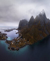 Luftaufnahme von ruhigen Wasser des Meeres waschen Insel mit felsigen Formationen unter bewölktem Himmel mit kleinen Dorf in Rein, Lofoten in Norwegen - ADSF33888