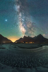 Scenic landscape of rocky cliffs under starry sky at dusk and village houses on coast of North Sea on Lofoten island - ADSF33922