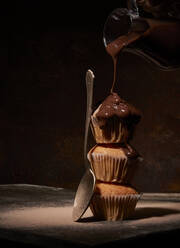 Süße Schokolade gießen auf leckere nackte Muffins serviert auf einander in der Nähe Löffel auf schwarzem Hintergrund im Zimmer - ADSF33950