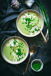 Top view of bowls with creamy pea soup served on table with black napkins and green onion near spoon in kitchen - ADSF33953