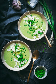 Draufsicht auf Schüsseln mit cremiger Erbsensuppe, serviert auf einem Tisch mit schwarzen Servietten und grünen Zwiebeln in der Nähe des Löffels in der Küche - ADSF33953