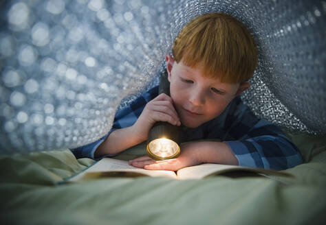 Boy (8-9) reading book under bed covers - TETF01270
