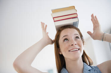 Teenage girl (14-15) holding stack of books on head - TETF01280