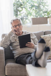 Älterer Mann sitzt auf der Couch im Wohnzimmer und benutzt einen Tablet-PC - TETF01284