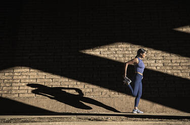 Frau streckt sich in der Nähe einer Backsteinmauer im Sonnenlicht - TETF01298