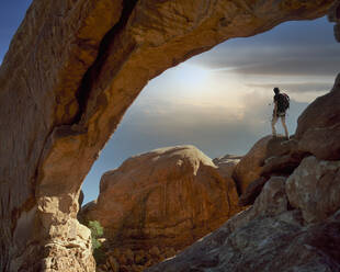 USA, Utah, Arches National Park, Climber under rocky arch at sunset - TETF01309