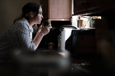 Woman looking through kitchen window - TETF01343