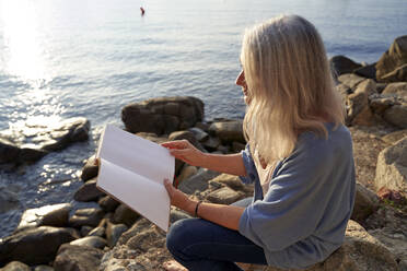 Frau liest Buch am Strand an einem sonnigen Tag - VEGF05396
