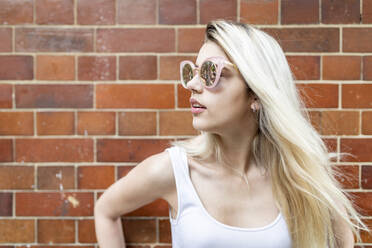 Teenager-Mädchen mit Sonnenbrille vor einer Backsteinmauer stehend - WPEF05828