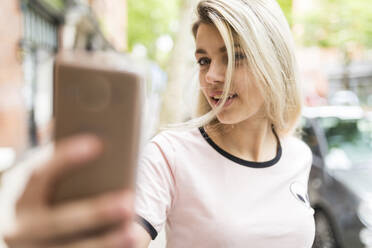 Teenager mit blondem Haar, der ein Selfie über sein Handy macht - WPEF05832