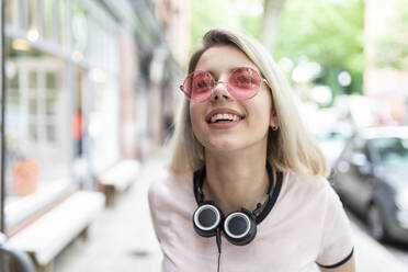 Fröhlicher Teenager mit drahtlosen Kopfhörern und Sonnenbrille - WPEF05833