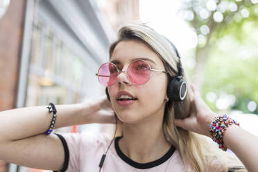 Teenage girl with hand in hair listening music through wireless headphones - WPEF05834