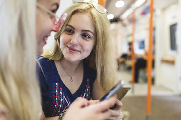 Lächelnder blonder Teenager mit Blick auf einen Freund, der ein Smartphone hält - WPEF05841