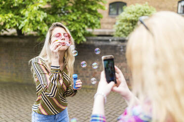 Teenager fotografiert Freund beim Ausblasen von Seifenblasen mit dem Smartphone - WPEF05842