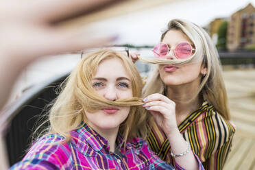 Smiling blond teenagers making mustaches with hair taking selfie - WPEF05849