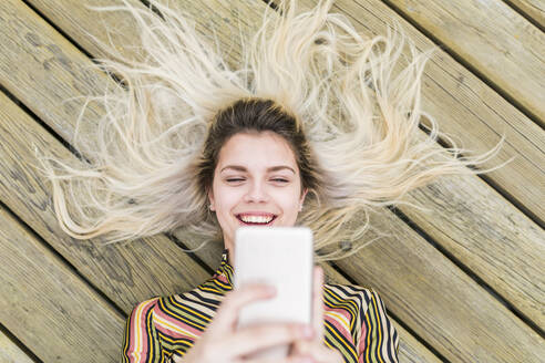 Fröhlicher Teenager, der ein Selfie durch ein auf dem Boden liegendes Mobiltelefon macht - WPEF05851
