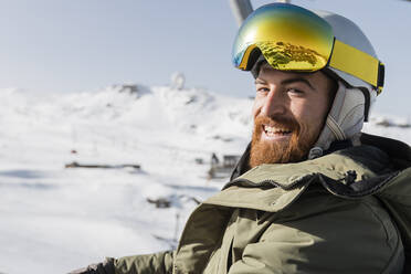 Smiling man wearing ski helmet and goggles on sunny day - JRVF02825
