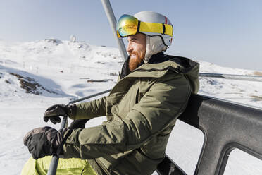 Lächelnder junger Mann, der im Skiliftsessel sitzt - JRVF02826