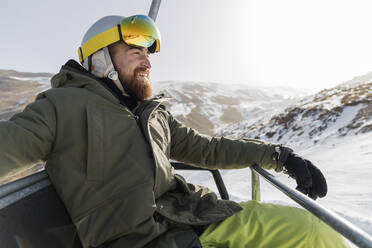 Lächelnder junger Mann mit Bart auf dem Skilift sitzend - JRVF02830