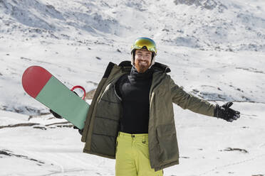 Glücklicher junger Mann mit ausgestreckten Armen auf einem schneebedeckten Berg stehend - JRVF02836