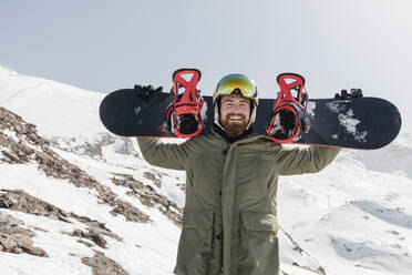 Glücklicher junger Mann trägt Snowboard auf den Schultern - JRVF02840