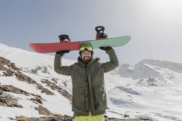 Lächelnder junger Mann, der ein Snowboard auf dem Kopf trägt - JRVF02842
