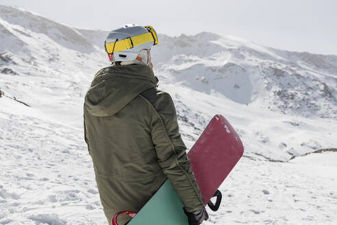 Junger Mann mit Snowboard auf einem schneebedeckten Berg stehend - JRVF02847