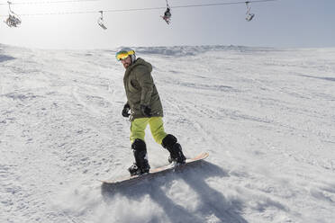 Junger Mann beim Snowboarden auf einem schneebedeckten Berg - JRVF02853