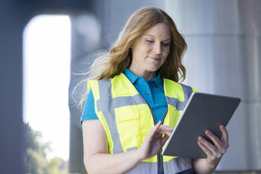 Smiling technician wearing protective workwear using tablet PC in industry - FKF04628