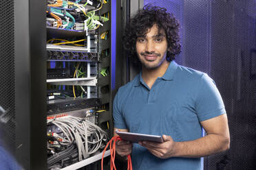 Smiling IT support holding tablet PC standing in server room - FKF04659
