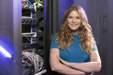 Happy technician standing with arms crossed in server room - FKF04662