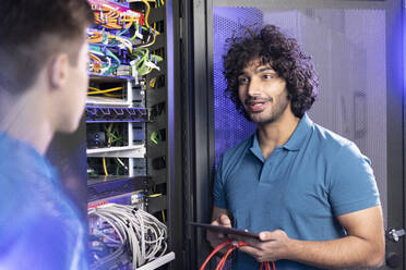 Technician holding tablet PC discussing with trainee in server room at industry - FKF04667