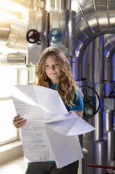 Smiling technician analyzing blue print standing in factory - FKF04669